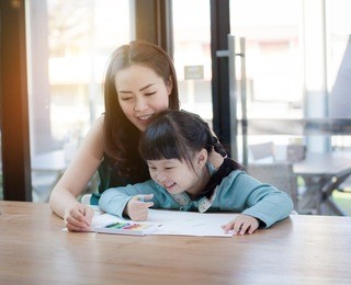 asian mother and daughter are having fun while drawing at home.mother and her child colors together