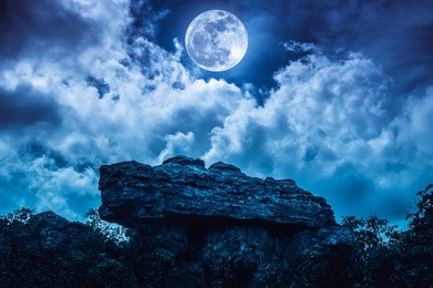boulder with blue sky background and beautiful full moon behind cloud at night. outdoor at nighttime. beauty of nature use as background. the moon were not furnished by nasa.