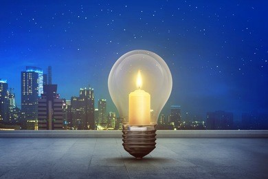 burning candle inside light bulb on floor with modern city background
