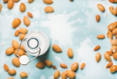 dairy alternative milk. almond milk in bottle and fresh nuts over blue background, top view, selective focus, copy space. clean eating, dairy-free, vegan, detox, allergy-friendly, healthy food concept