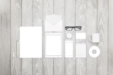 stationary mock-up includes paper, sketchbook, tablet, smart phone, business card, pen, glasses, compact disk, mug and badge pin on white wood background.