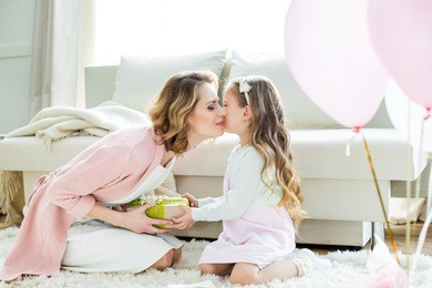 adorable little girl presenting gift and kissing happy mother on mothers day