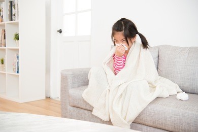 little girl sick  blowing her nose with tissue and cover with blanket sitting on sofa in the living room at home. family activity concept.