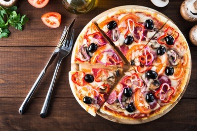sliced italian pizza with salami, mushroom, tomatoes, sweet pepper, black olives and purple onion on dark wooden background top view. italian traditional food. popular street food.