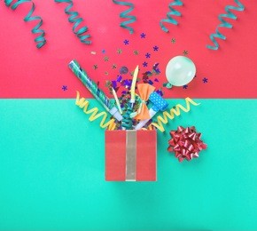 red gift box with various party confetti, balloons, streamers, noisemakers and decoration on a multicolored background. top view