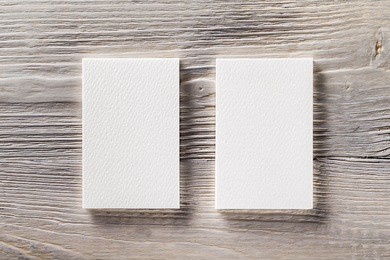 closeup mockup of two blank vertical business cards at light natural wooden background.