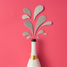 white champagne bottle with silver glittering splashes on pink background. flat lay. minimal party concept.