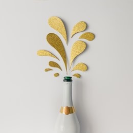 champagne bottle with golden glittering splashes on white background. flat lay. minimal party concept.