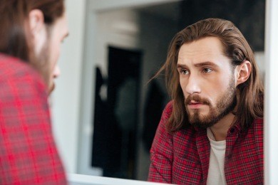 handsome bearded young man in plaid shirt looking at the mirror at home