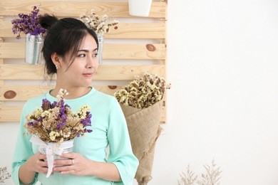 smiling portrait of an attractive florist business asian woman owner at a flower shop market working and making a new floral arrangement during a sunny day. small business owner.