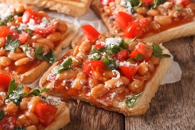 toasts with beans in a tomato sauce, cheese and herbs closeup on the table. horizontal
