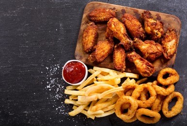 fast food products : onion rings, french fries and fried chicken on dark table, top view