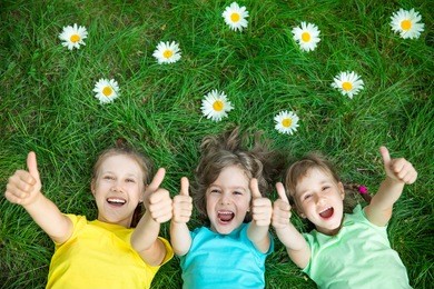 group of happy children playing outdoors. kids having fun in spring park. friends lying on green grass. top view portrait