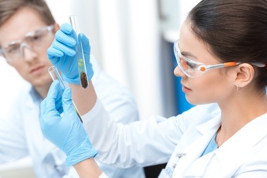 young woman scientist in protective glasses holding test tubes with soil and plants