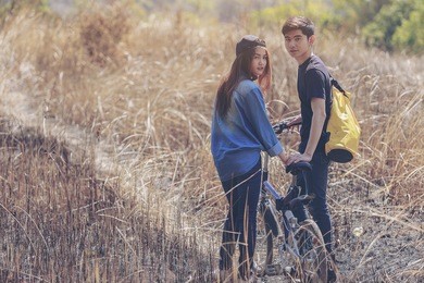 couple of romantic lovers sitting on  bike in nature . asian handsome man and beautiful girl is travel , hipster people,young asian couple, standing with bicycles on mountain and forest 