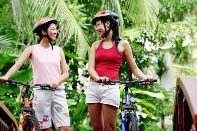 two women standing with bicycles, smiling at each other