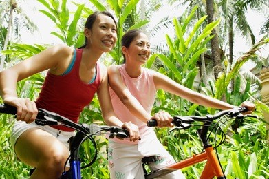 two girls smiling and riding bikes through a park