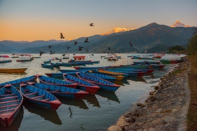 sunrise with wooden boats on phewa lake, pokhara, nepal.