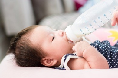 portrait of a little adorable infant baby girl lying on back on breadfeeding pillow and eating milk from bottle