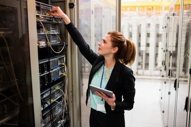 technician holding digital tablet while examining server in server room
