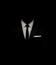man in a black suit and white shirt and black tie on a black background. without a face. the businessman in the dark. studio shot