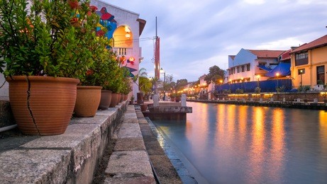 malacca river at the evening time. light of street lanterns reflecting in the river. colorful houses on both sides of the river. flowers in a clay pot on the left side of the river. travel malaysia