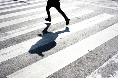 blurry child's legs and kid's shadow with a backpack, on crossing while running over the street