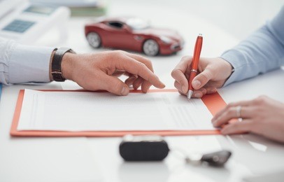 woman signing a car insurance policy, the agent is pointing at the document