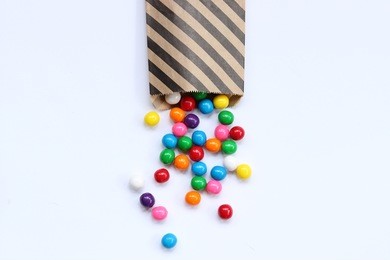 bright gumballs spill out of a black striped treat bag onto white empty space for copy.