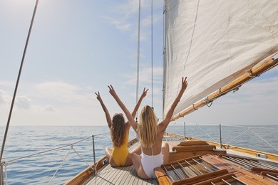 beautiful women friends celebrate arms raised peace sign on sailboat in ocean on luxury lifestyle happy adventure travel vacation