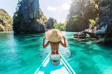back view of the young woman in straw hat relaxing on the boat and looking forward into lagoon. travelling tour in asia: el nido, palawan, philippines.