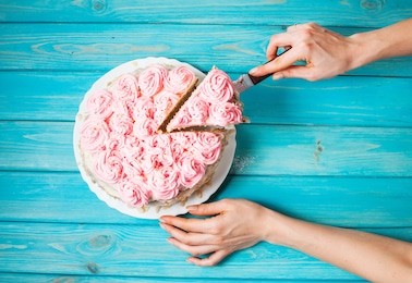 woman's hands cut the cake with pink cream on blue wood background. pink cake. top view