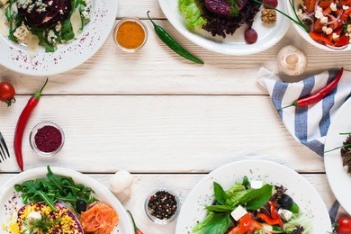 fresh vegetable salads frame flat lay. top view on white wooden table with free space for text between side dish buffet. vegetarian cuisine, menu concept