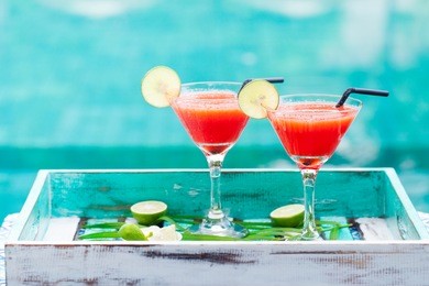 strawberry margarita cocktail on colorful wooden background with palm leaf.