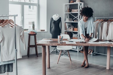 working on new design. full length of young african woman drawing using pencil and looking at paper while standing in her workshop 