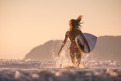 woman runs into the ocean with surfboard