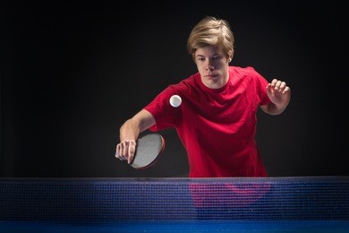 young man tennis player in play on black background