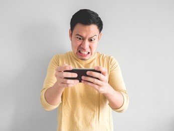 angry asian man plays mobile game on his smartphone.