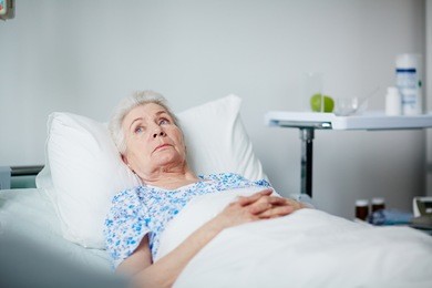lonely senior woman lying thoughtful on white sheets in hospital ward
