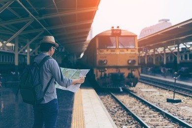 young man traveler with sky blue backpack and hat looking the map with train background at train station bangkok. traveling in bangkok thailand. travel concept 
