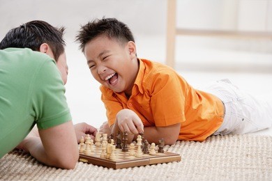 father and son lying on floor, playing chess, laughing
