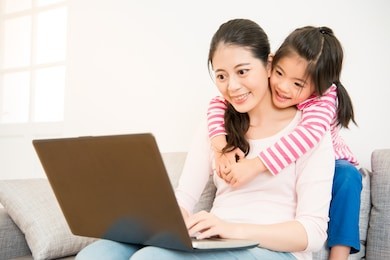 good relationship mother and little cute girl daughter looking at laptop together seated on sofa in the living room at home. family activity concept.