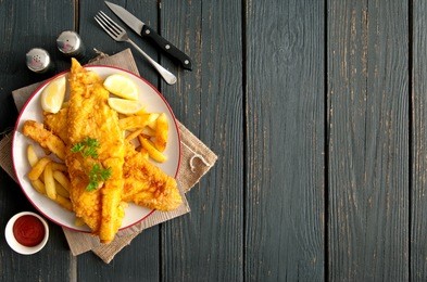 two pieces of battered fish on a plate with chips on a wooden table with space 