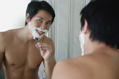 man shaving, looking at camera through mirror reflection