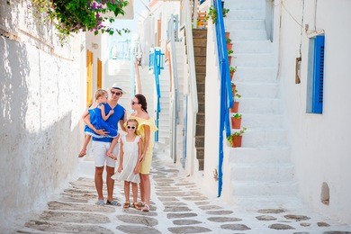 family vacation in small european city. parents and kids at street of greek traditional village on mykonos island