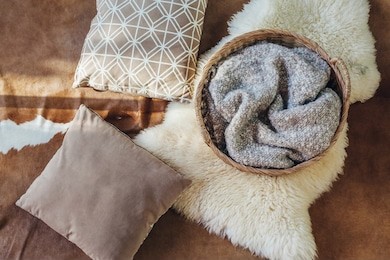 wicker storage basket with woolen blanket inside and cushions on sheep carpet, top view from above. natural and organic interior decor.
