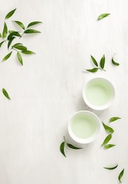 tea concept, two white cups of tea surrounded with green tea leaves, view from above, space for a text