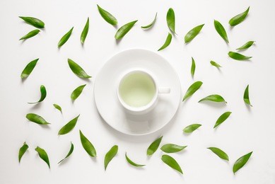 cup of fresh green tea with green leaves around it, view from above
