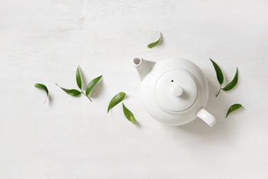 tea concept, teapot with tea surrounded with green tea leaves, view from above