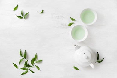 tea concept, two white cups of tea and teapot surrounded with green tea leaves, view from above, space for a text